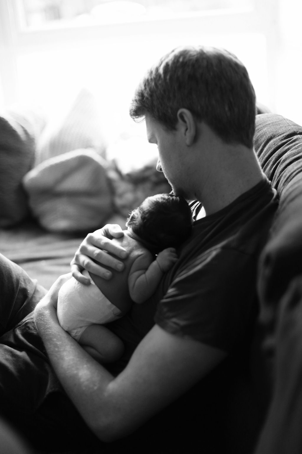 dad sitting on couch with his little new born baby on chest