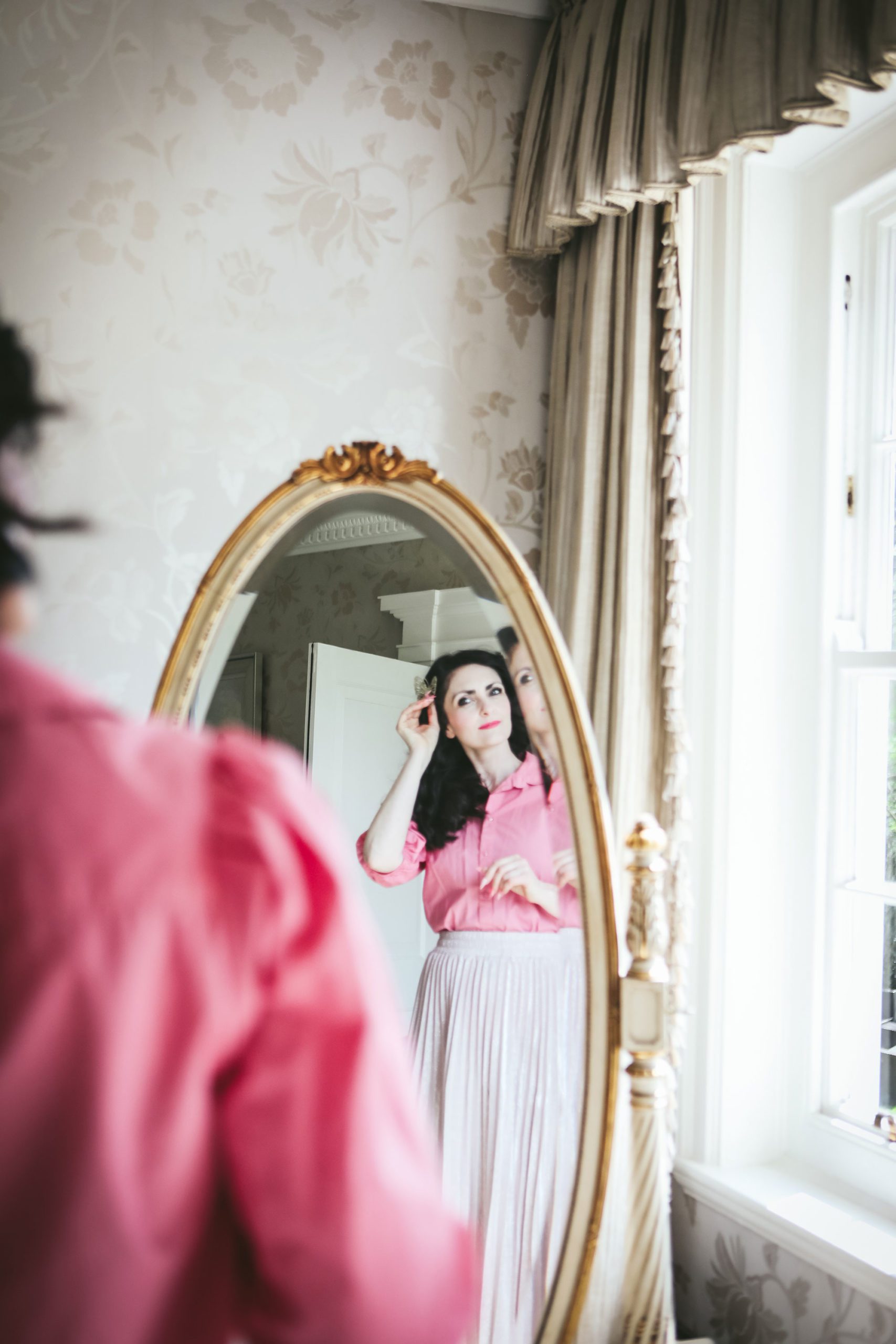 lady looking into a full length mirror with a pink blouse and white skirt